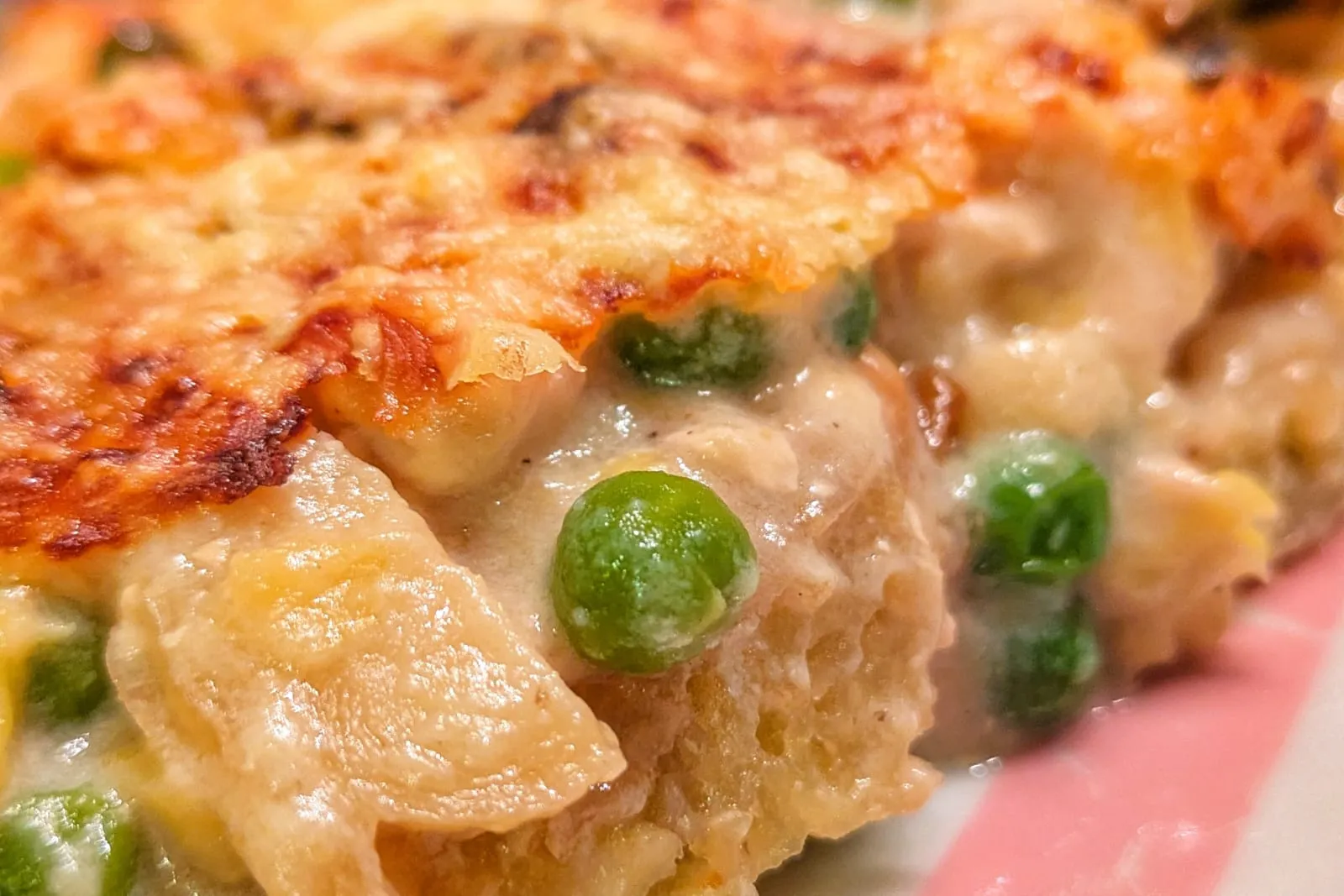 Gros plan sur un gratin de röstis au poulet, avec sa croûte de gruyère dorée et des petits pois qui dépassent de la sauce crémeuse.
