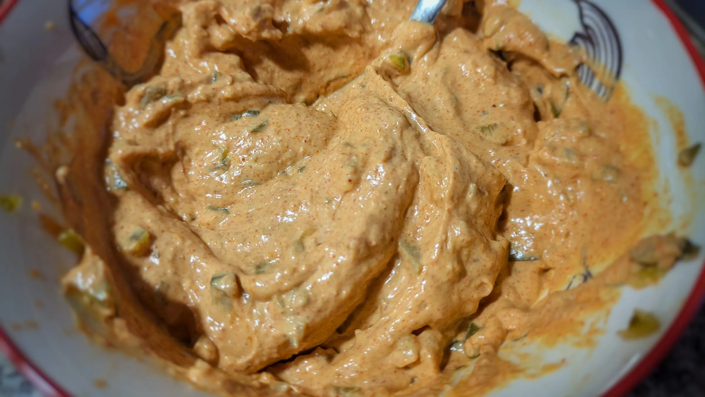 Une sauce burger crémeuse et orangée, parsemée de morceaux de cornichons, dans un bol.