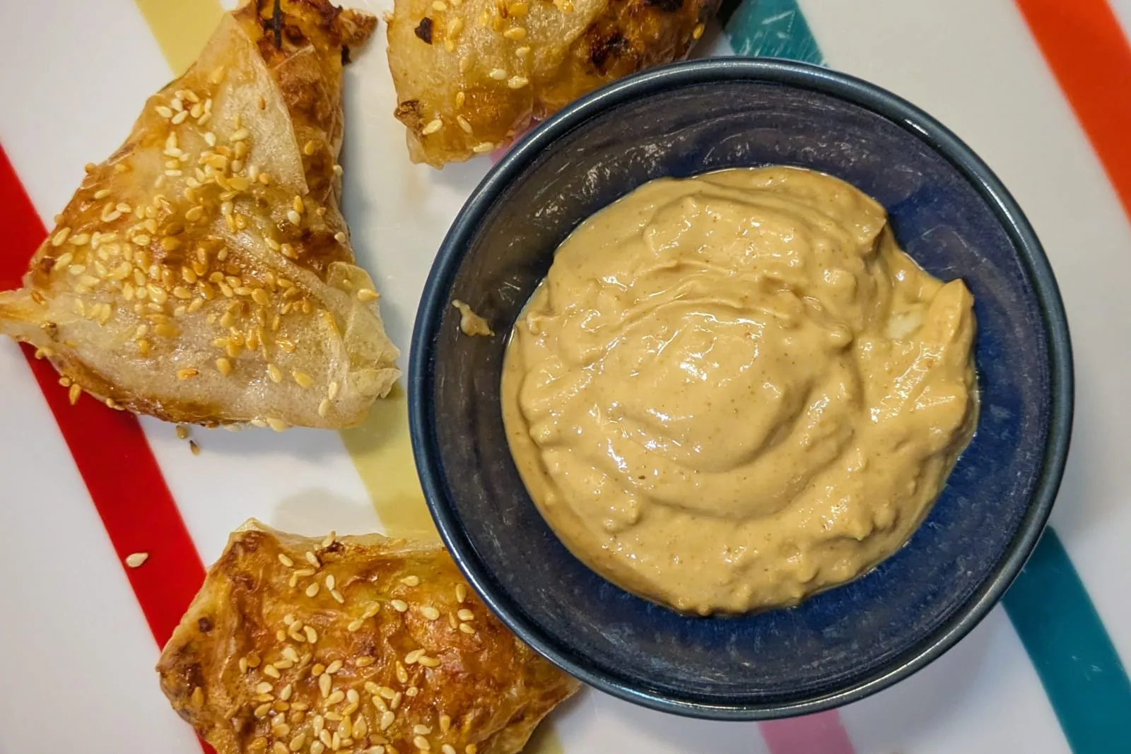 Des croustillants de poulet dorés en forme de triangle avec des graines de sésame, et une sauce cremeuse au milieu
