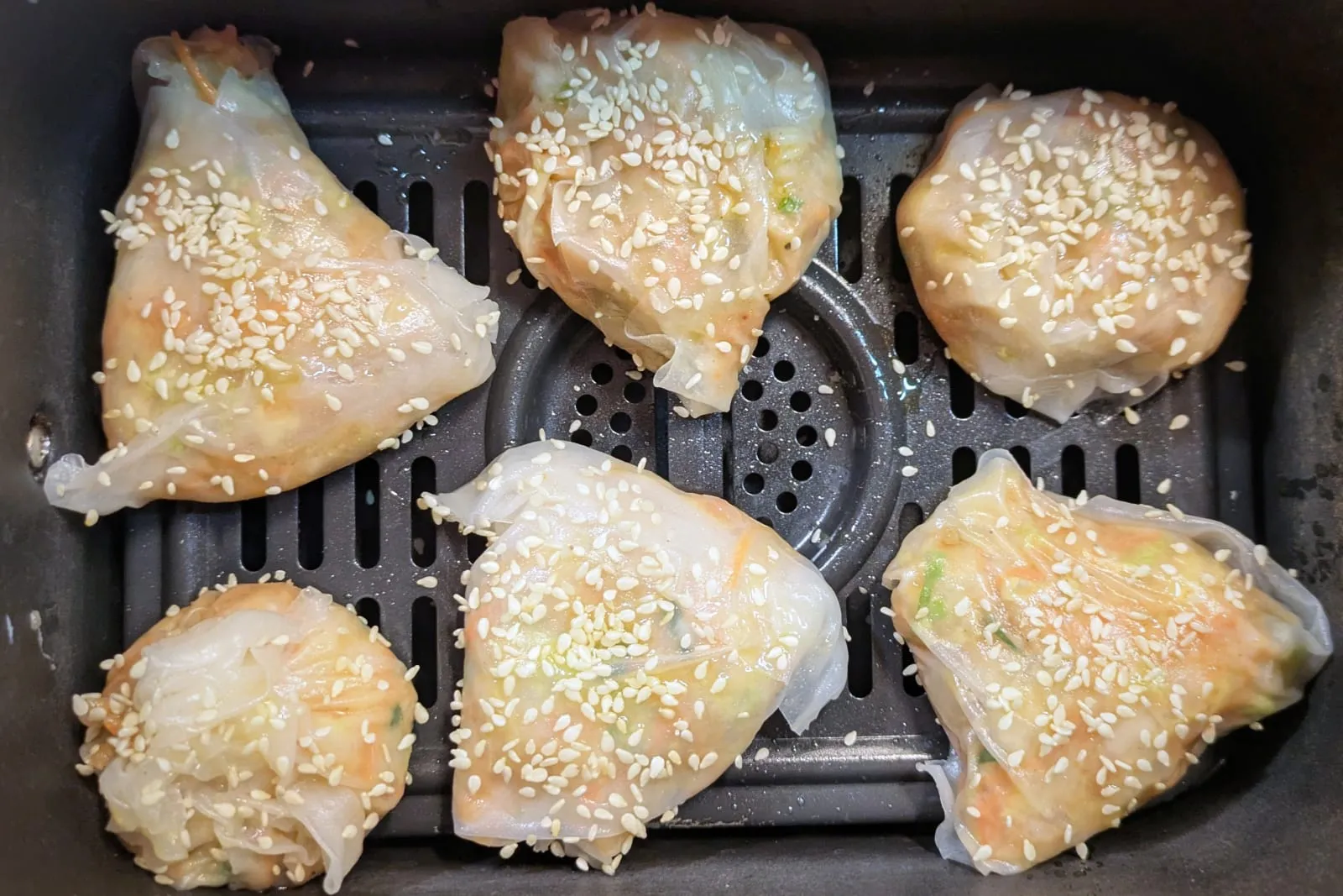 Des croustillants de poulet en feuilles de riz enrobés de graines de sésame, disposés sur du papier sulfurisé dans un bac d'airfryer.